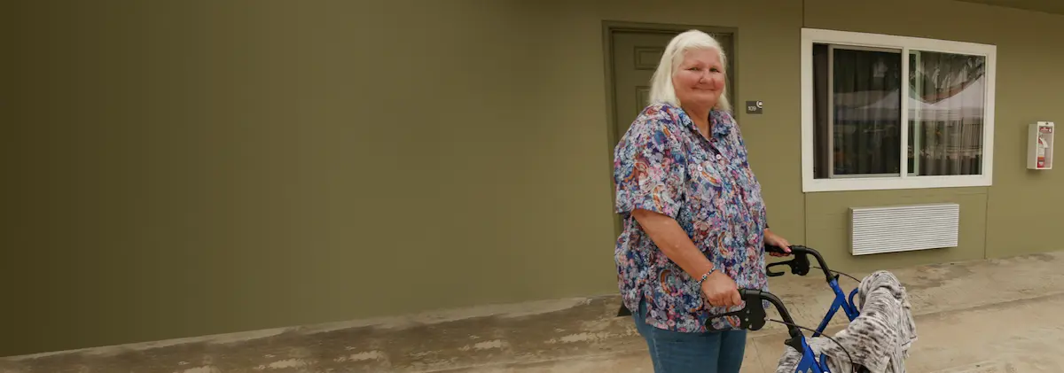 woman with walker smiling in front of her new apartment.