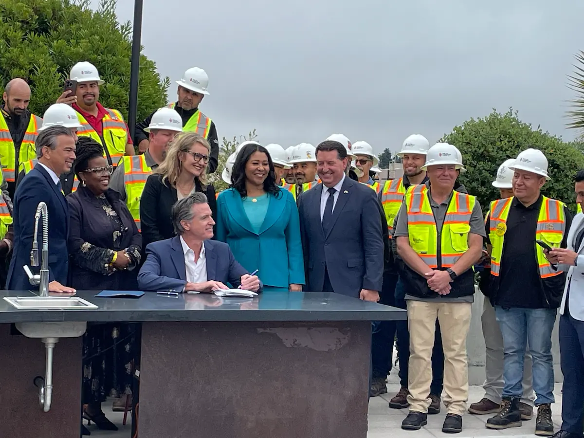 Governor Gavin Newsom surrounded by dignitaries signing legislative housing bills.